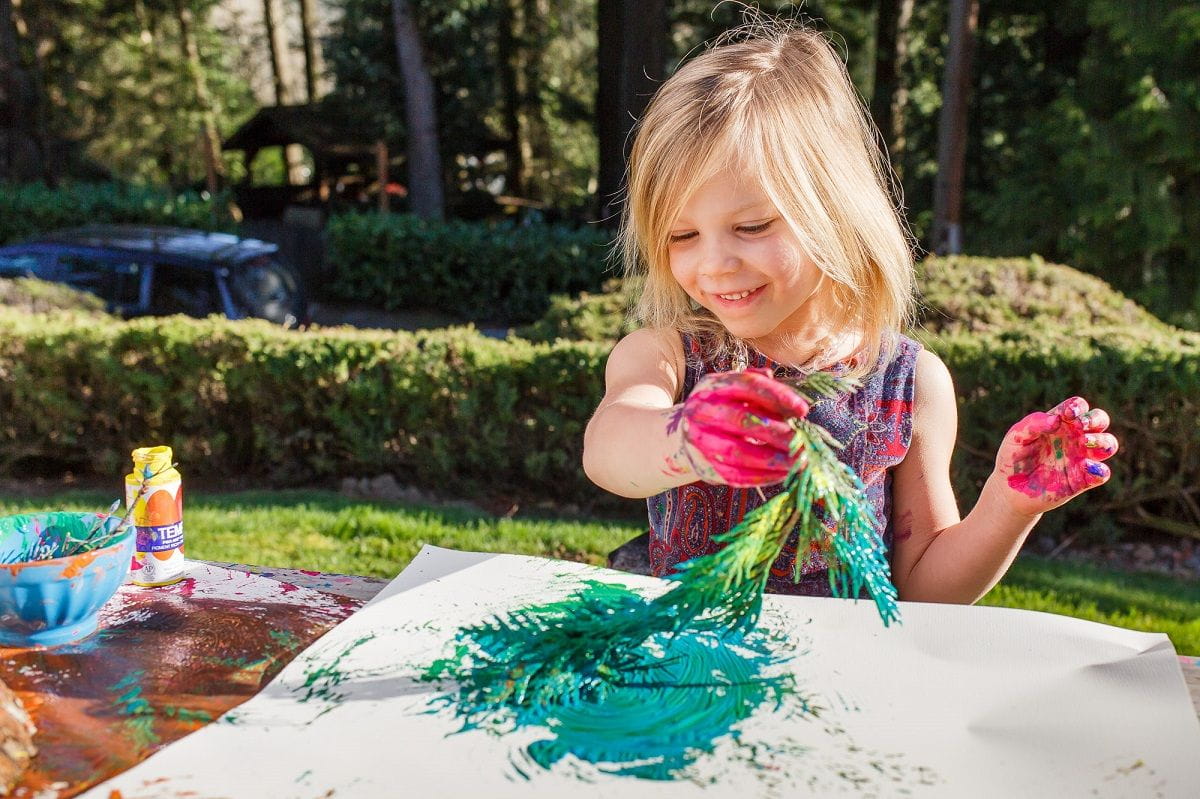 girl happily painting with a leafy tree branch