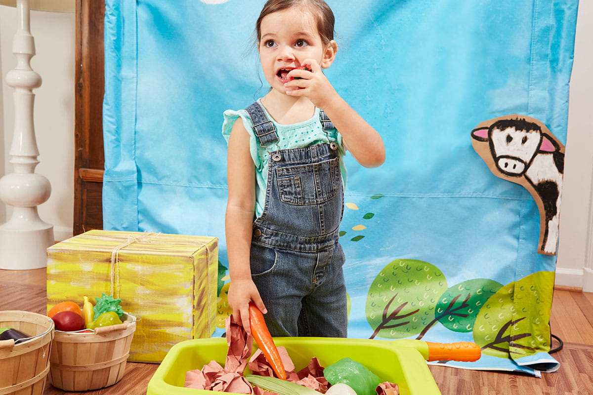 child in overalls play food wheelbarrow