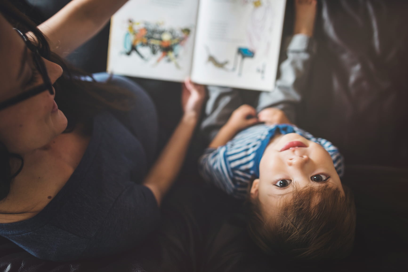 mom reading to boy as he looks up at camera Stocksy / 347620