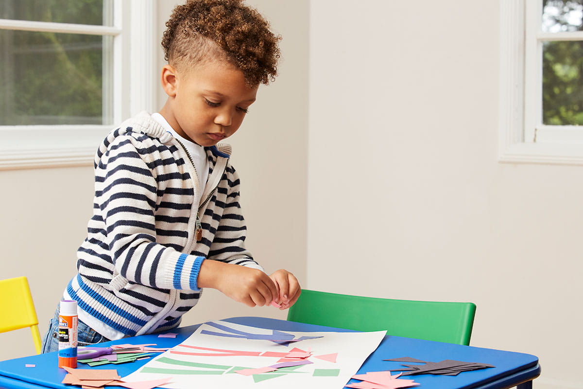 Wide shot of boy pasting geometric paper shapes onto paper