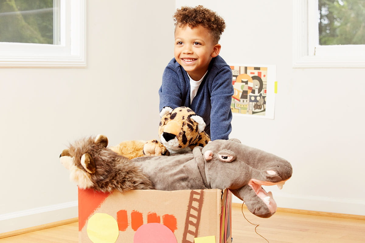 Happy child put animals in cardboard tugboat