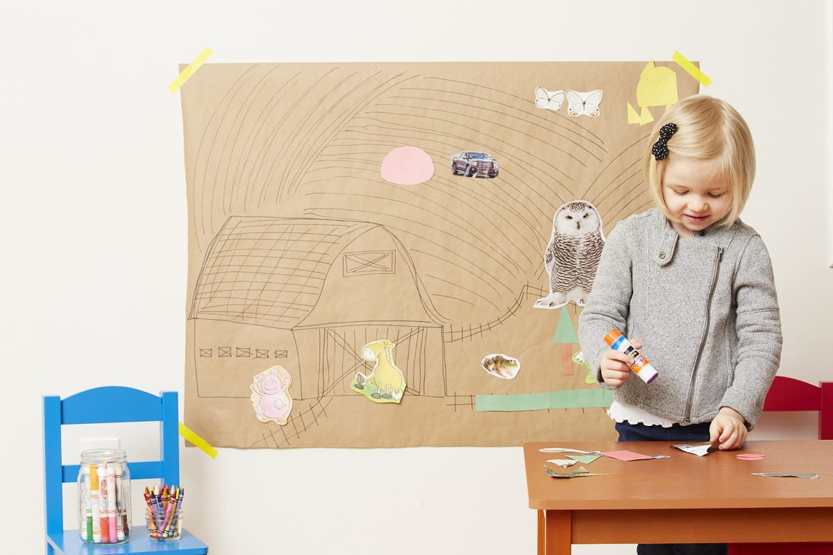 Toddler glues pictures on wall mural