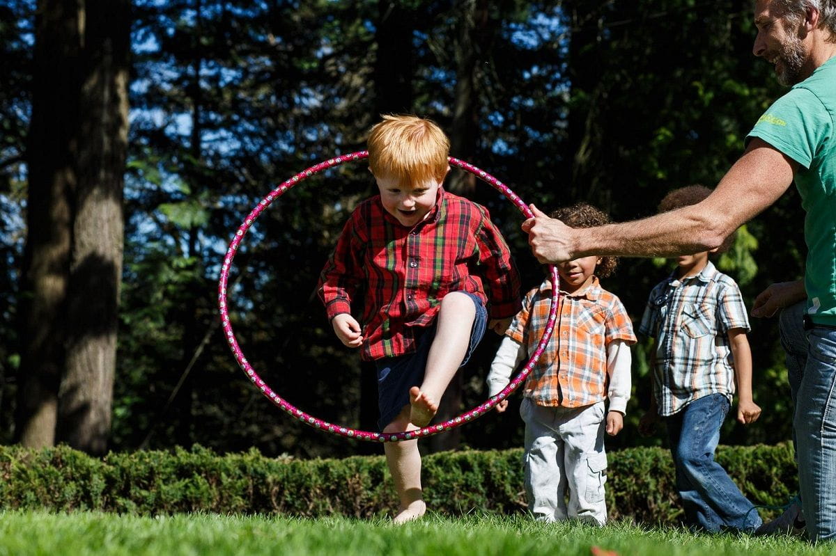 boy jumping through hula hoop held by adult