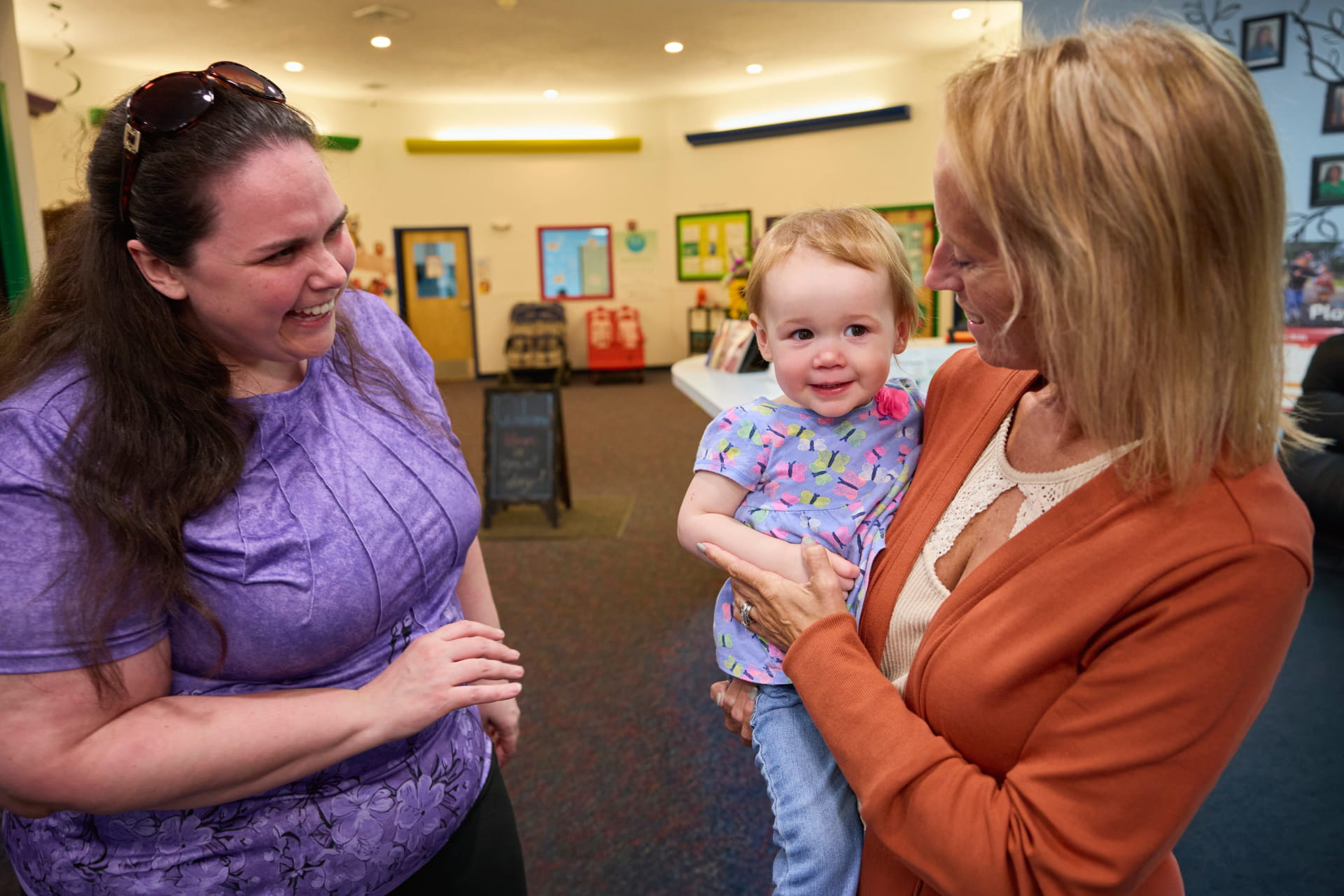 A teacher and a caregiver holding a toddler talking together at classroom pickup