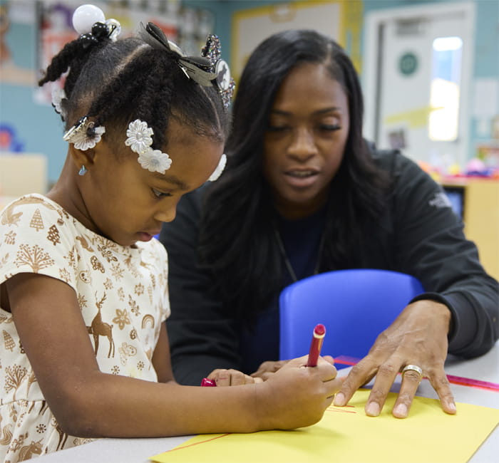 teacher helping kindergartener write with marker