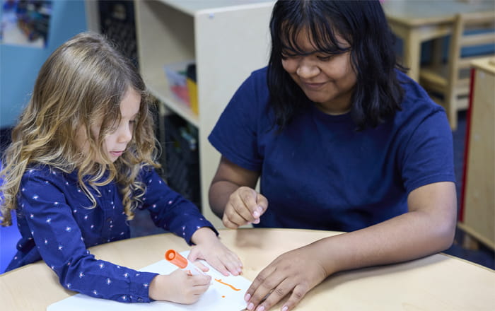 teacher helping kindergartener write with marker