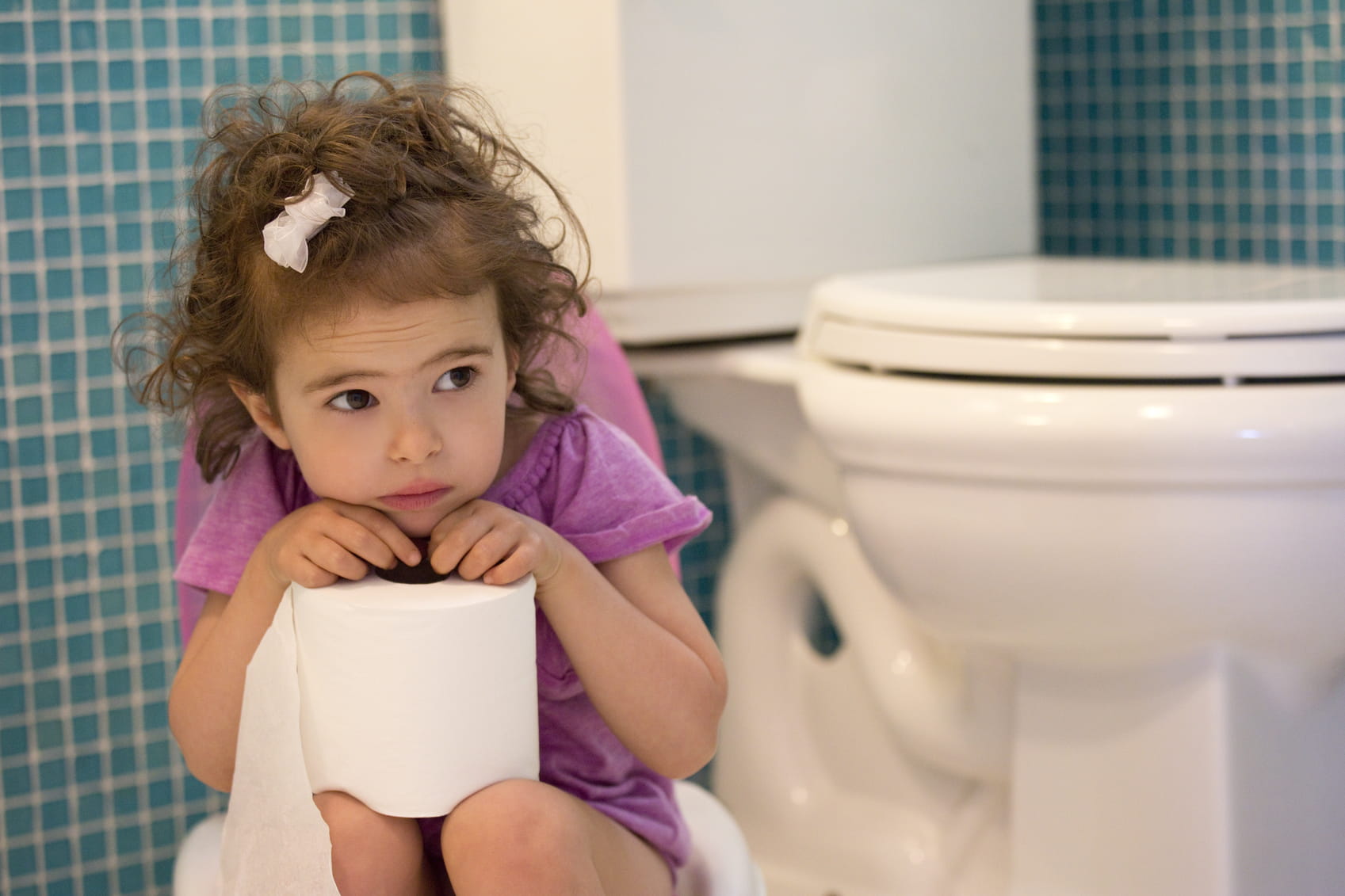 little girl in a purple dress sitting in front of the toilet with toilet paper 